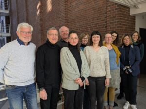 11 Menschen unterschiedlichen Alters, die lächelnd als Gruppe in die Kamera blicken