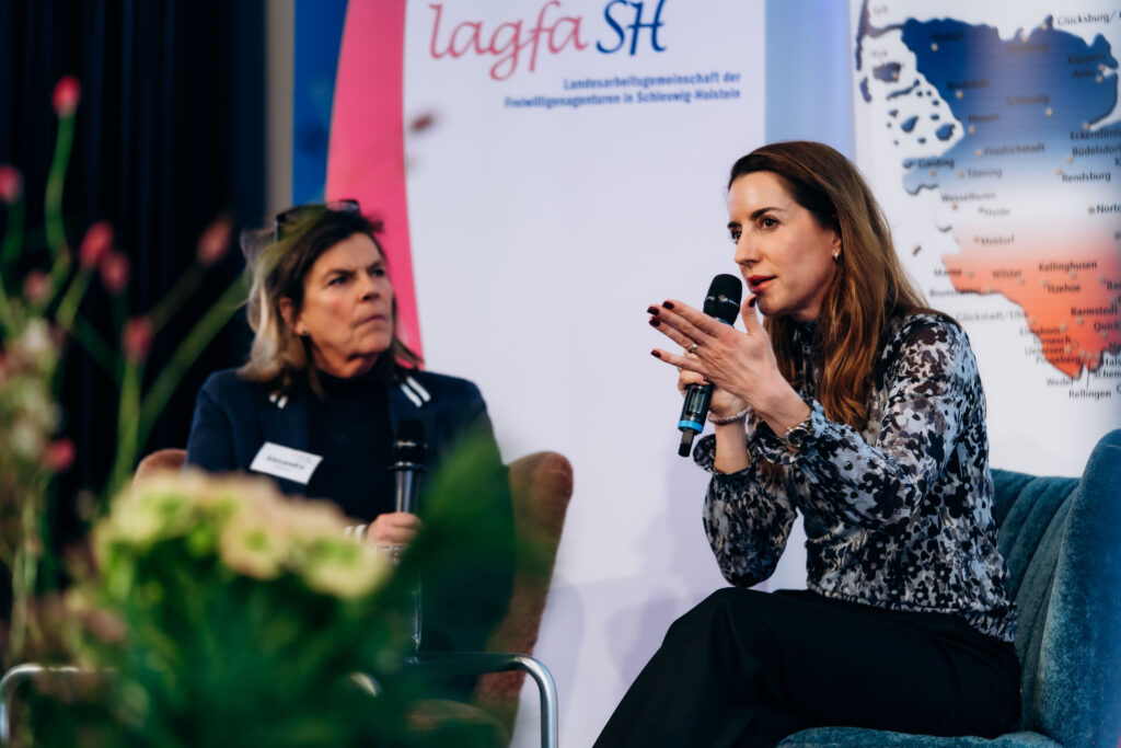 Frau erklärt mit Mikro in der Hand vor lagfa SH Logo