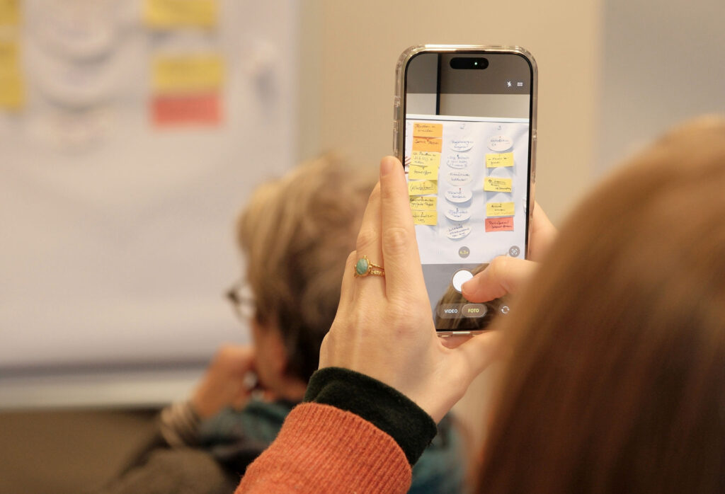 Detailaufnahme von Handy, das Moderationskarten fotografiert