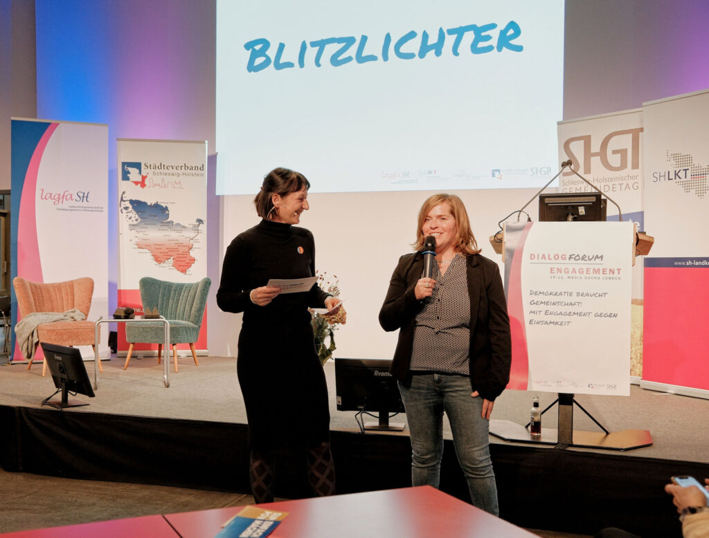 Zwei Frauen mit Mikros vor der Bühne mit Projektion "Blitzlichter"