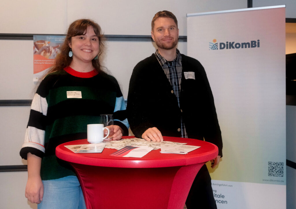 Eine junge Frau und ein junger Mann stehen am Stehtisch und lächeln den Betrachter an