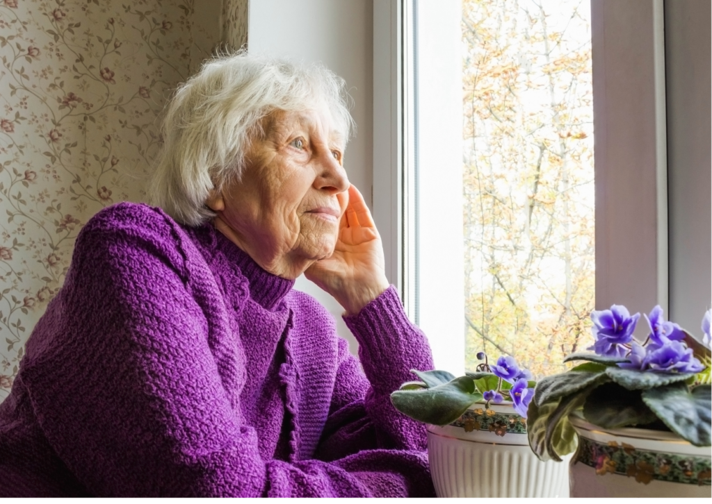 Alte Frau guckt nachdenklich aus dem Fenster